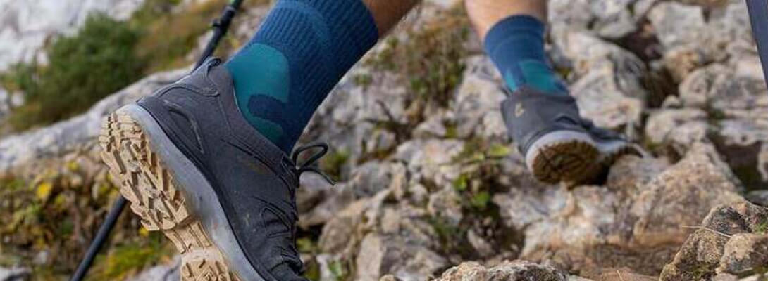 Medo-lengte merino wandelsokken tijdens het klimmen Persoon gaat een berg op over stenen en draagt medium -lengte wandelsokken