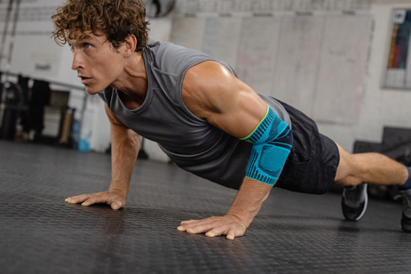 Jonge man met elleboogverband maakt push-ups op de vloer van een trainingsruimte
