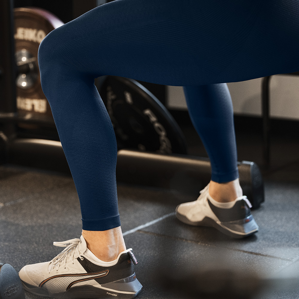 Stabiliteit vanaf de basis – Compressietights voor je beentraining Close-up van de benen van een sporter in blauwe compressietights tijdens een training in de sportschool. De tights ondersteunen stabiliteit en doorbloeding.