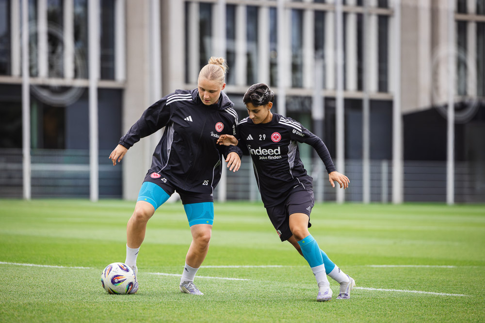 Twee speelsters van Eintracht Frankfurt in duel tijdens een training, allebei met compressiesleeves om de knieën.