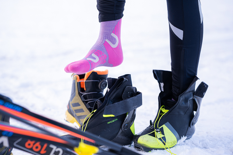 Perfecte voorbereiding voor langlaufen met de juiste uitrusting. Een close-up van een langlaufuitrusting: Een atlete trekt neonroze functionele sokken aan, terwijl naast haar hoogwaardige skischoenen en ski's in de sneeuw liggen.