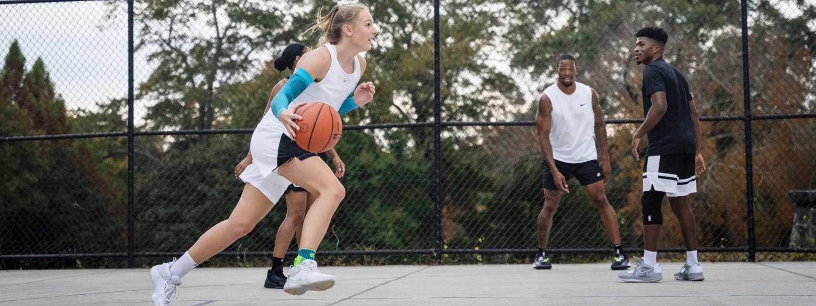 Druibberen met armmouwen in basketbal Basketbalspeler dribbelt langs haar tegenstanders op een vrije ruimte en draagt blauwe arm mouwen