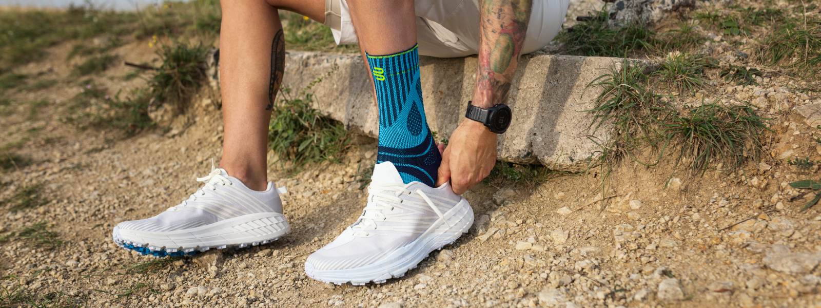 Ren nog veiliger en pijnvrij met achilles peesverband Man trekt een hardloopschoen op een steen op een steen over zijn achilles peesverband