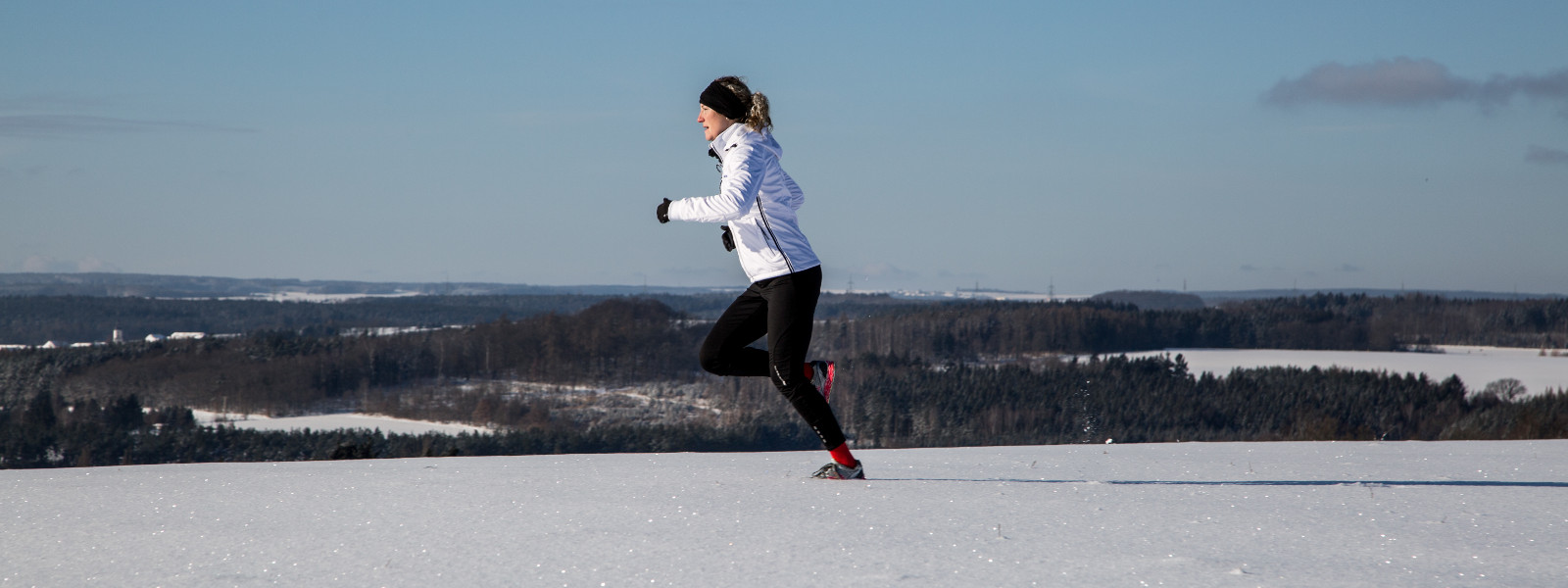 Vrouw in een wit hardloopjasje joggingen met zelfs sneeuwveld op de achtergrond, kleine bossen en open plek om te wisselen