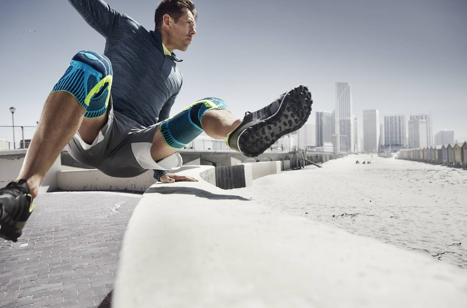 Mann met twee kniebanden springt over een obstakel bij Urban Running	 op de achtergrond van wolkenkrabbers