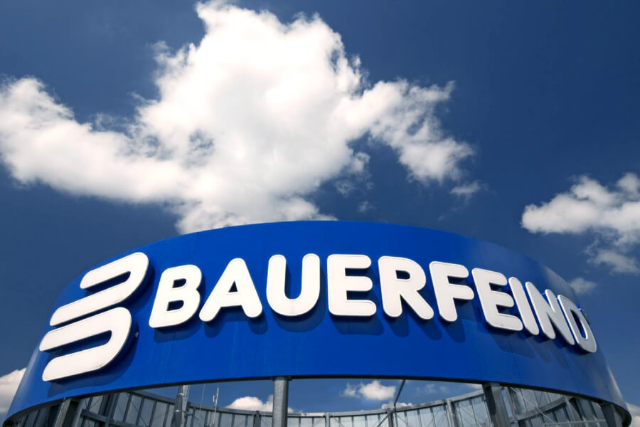 Het hoofdkantoor van Bauerfeind Company in Zeulenroda-Triebes Bauer vijandelijke belettering op een blauw oppervlak op het dak van een gebouw met een hoog opruiming erboven blauwe lucht met een wolk