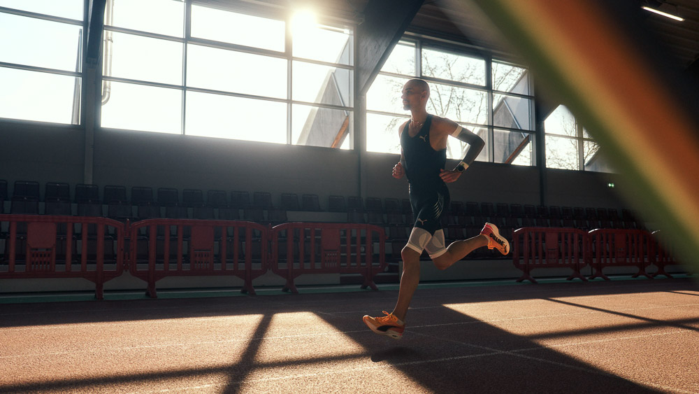 Marathonloper Hendrik Pfeiffer traint op een indoorbaan in tegenlicht, met compressie arm- en beensleeves voor extra stabiliteit en prestaties.