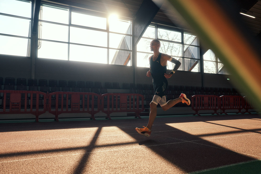 Marathonloper Hendrik Pfeiffer traint op een indoorbaan in tegenlicht, met compressie arm- en beensleeves voor extra stabiliteit en prestaties.