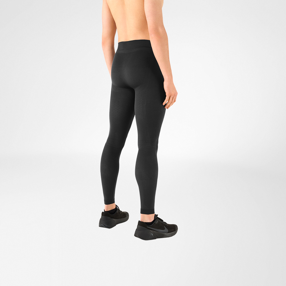 Je ziet een detail van een shirtloze man met zwarte sportschoenen en een antracietgrijze compressiebroek. Hij staat zijdelings met zijn rug naar de camera.