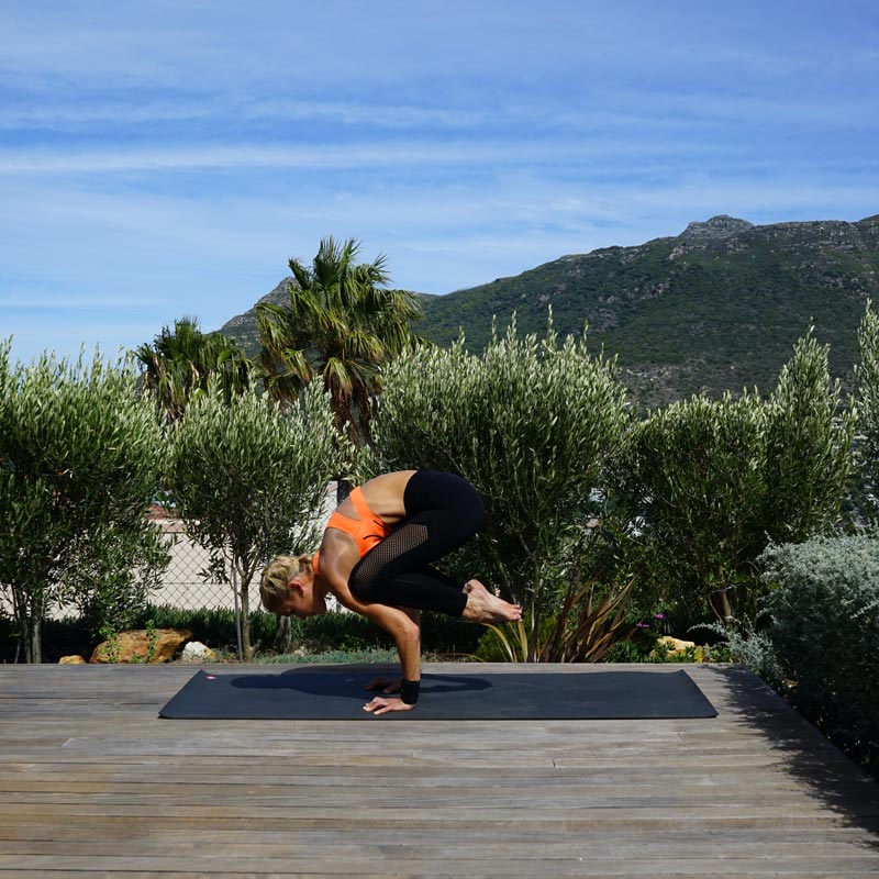 Vrouw maakt yoga in balans op haar terras op haar handen terwijl haar benen achter het bovenlichaam in de lucht hangen