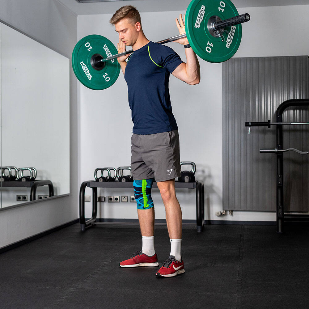 De man met een knie in de sportschool is een barbell in zijn nek voordat hij een squat uitvoert