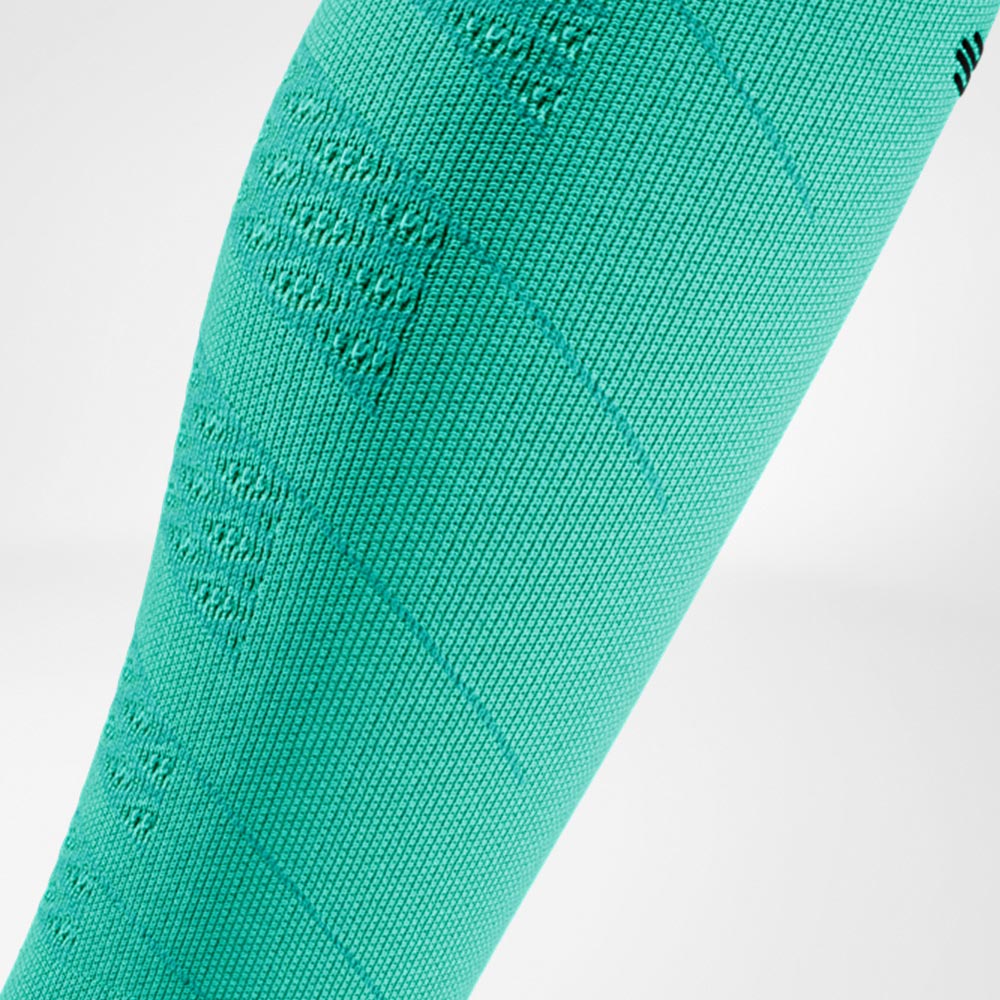 Detailopname van een groene Run Performance Compression Sleeve op het onderbeen, met duidelijk zichtbaar breiwerk dat zorgt voor gelijkmatige compressie en ondersteuning bij sportieve inspanning.