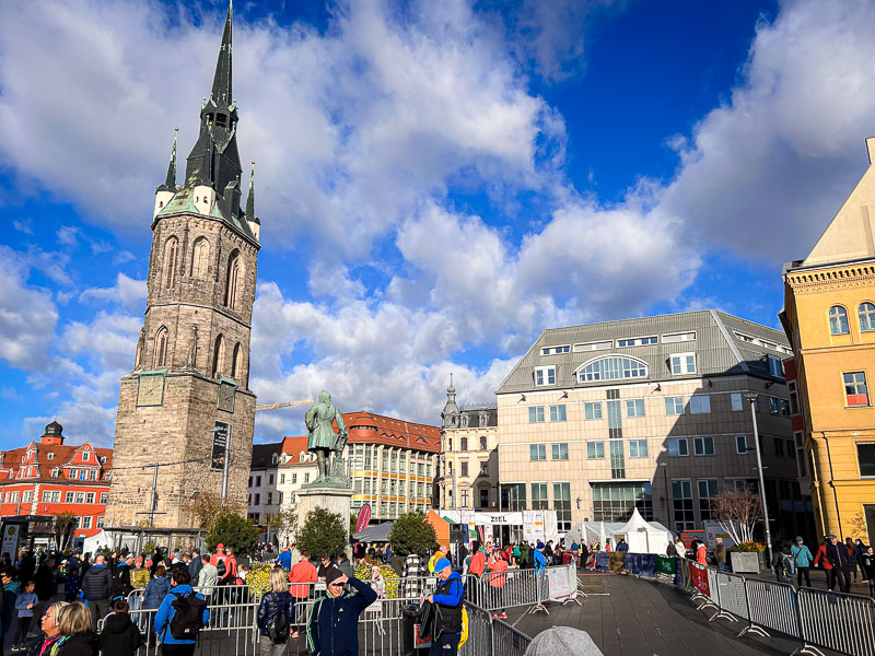 Het marktplein in Halle tijdens de Centraal-Duitse Marathon met de Rode Toren op de achtergrond. Lopers en toeschouwers verzamelen zich op het marktplein van Halle voor de start van de Centraal-Duitse Marathon. Op de achtergrond staat de iconische Rode Toren, een herkenningspunt van de stad.