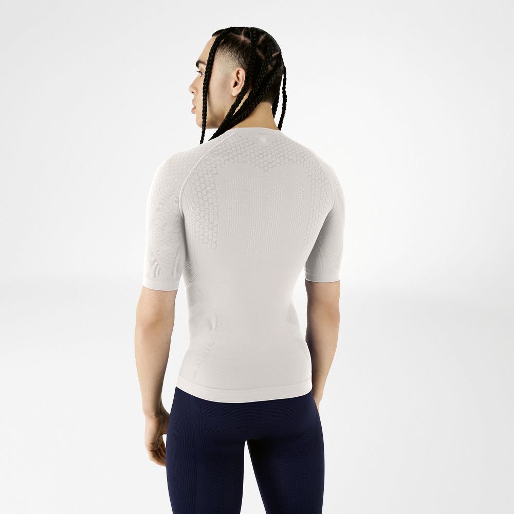 Een man draagt een zilvergrijs compressieshirt, staat met zijn rug naar de camera en kijkt over zijn schouder.