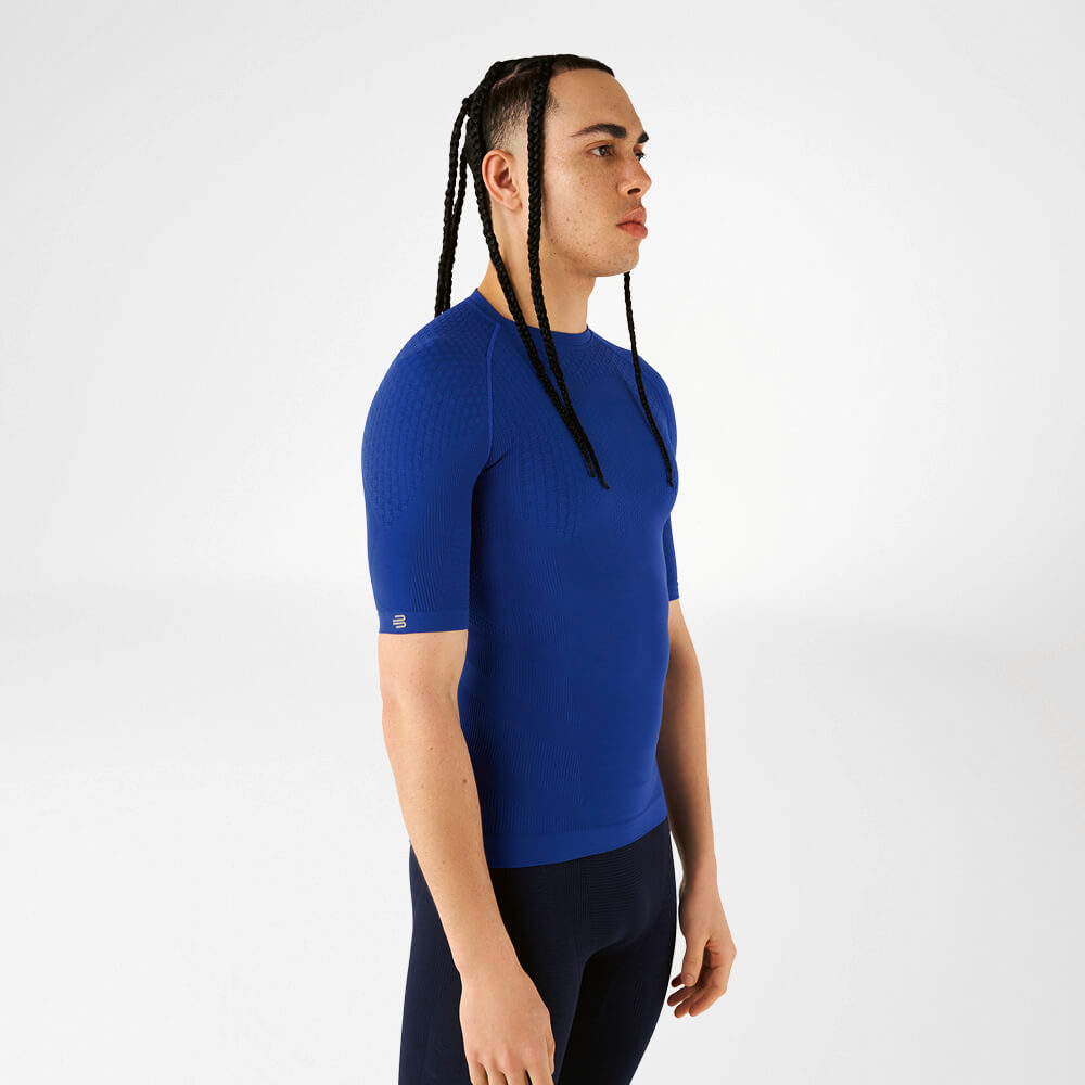 Een man draagt een blauw compressieshirt, staat zijwaarts en kijkt vooruit.