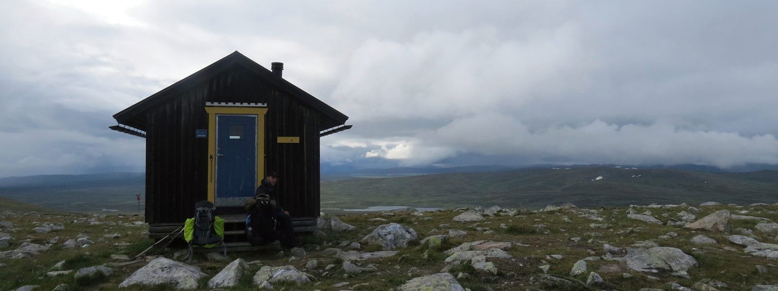 Een eenzame hut in de bergen in het midden van grove weiden met kleine rotsen op de achtergrond de dichte wolkenkap en een klein bergmeer