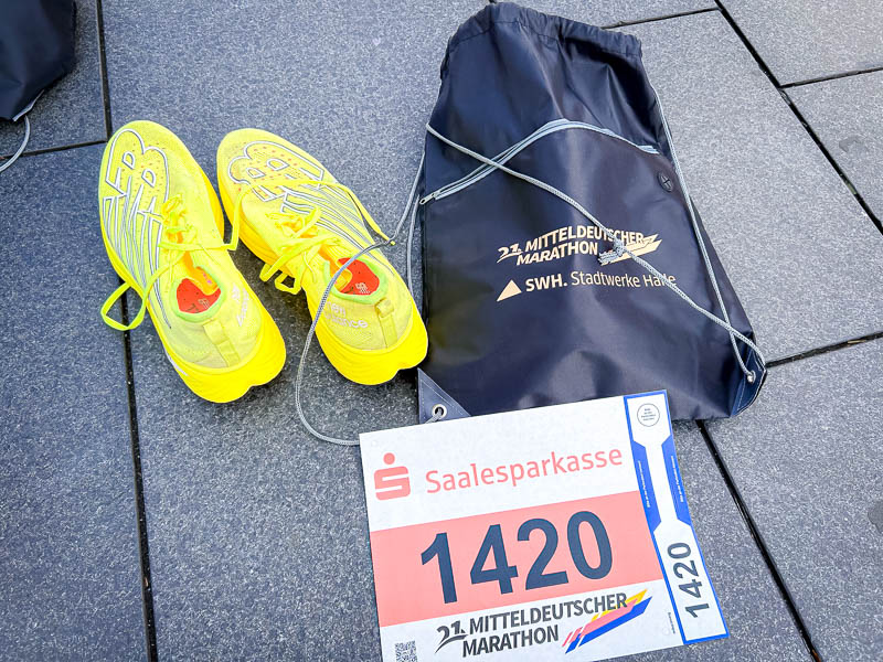 Halve marathon-uitrusting - Startnummer en hardloopschoenen op racedag Racedag bij de halve marathon: Gele hardloopschoenen naast het startnummer en een sporttas van de 21e Mitteldeutscher Marathon, klaar om te gaan.