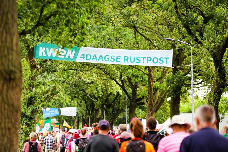 Rustpunt tijdens de 4Daagse Talloze deelnemers passeren een rustpunt tijdens de 4Daagse. Boven hen hangt een groot spandoek met de tekst "KWBN 4DAAGSE RUSTPOST".