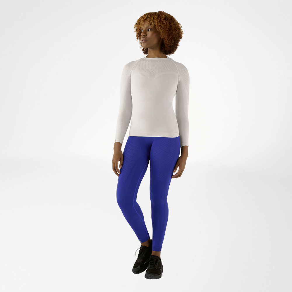 Vrouw in een zilvergrijs, nauwsluitend langmouwshirt en blauwe compressiebroek, vooraanzicht