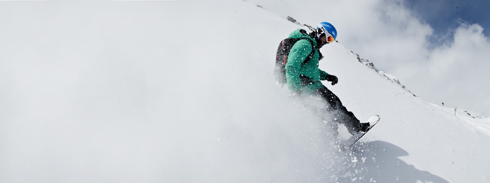 Snowboarders met een groene jas wervelt sneeuw waarop de hele linkerkant van de foto wit verven tijdens het remmen