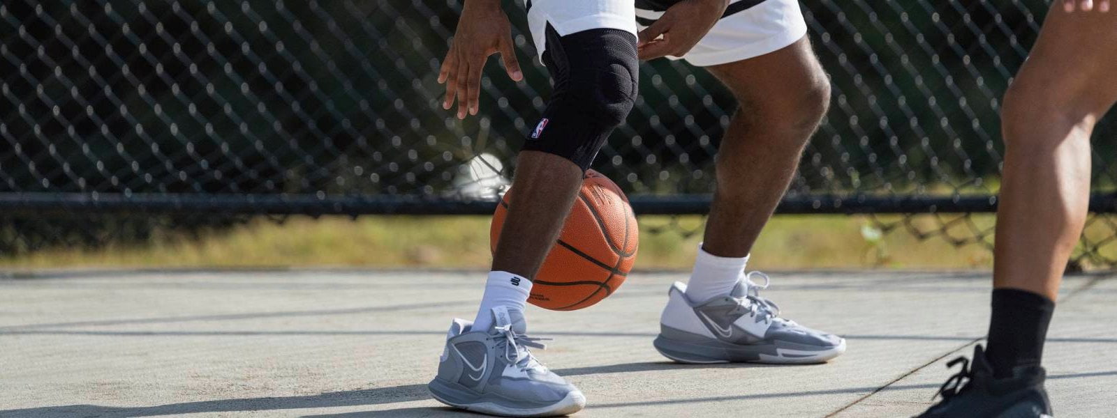 Kniesteun NBA bij basketbal Speler dribbelt op een straatbalveld met een basketbal en draagt een zwarte NBA -knieondersteuning