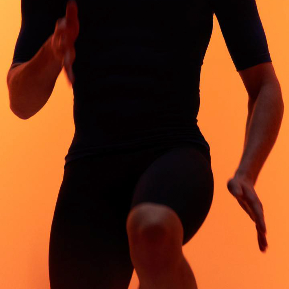 Fitnessoefeningen met de nieuwe Bauerfeind compressiekleding Een man in sportkleding doet een kniehef voor een oranje achtergrond