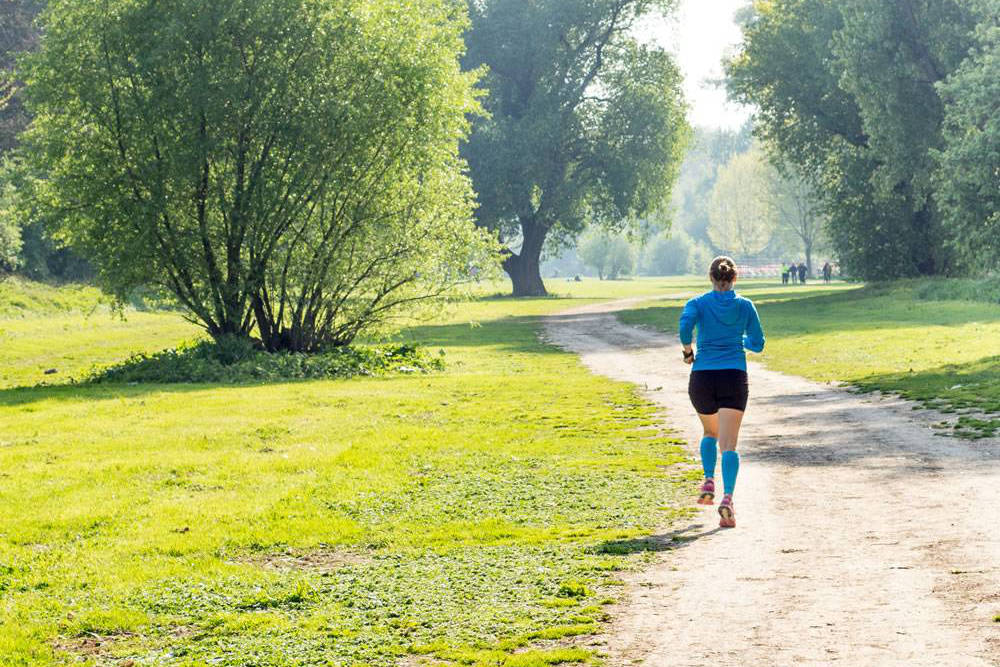 Vrouw met een blauwe trui en blauwe waden-mouwen rennen door het park	 achteraanzicht