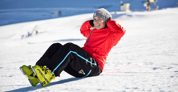 Ski-loper in een rode jas maakt een sit-up in de sneeuw