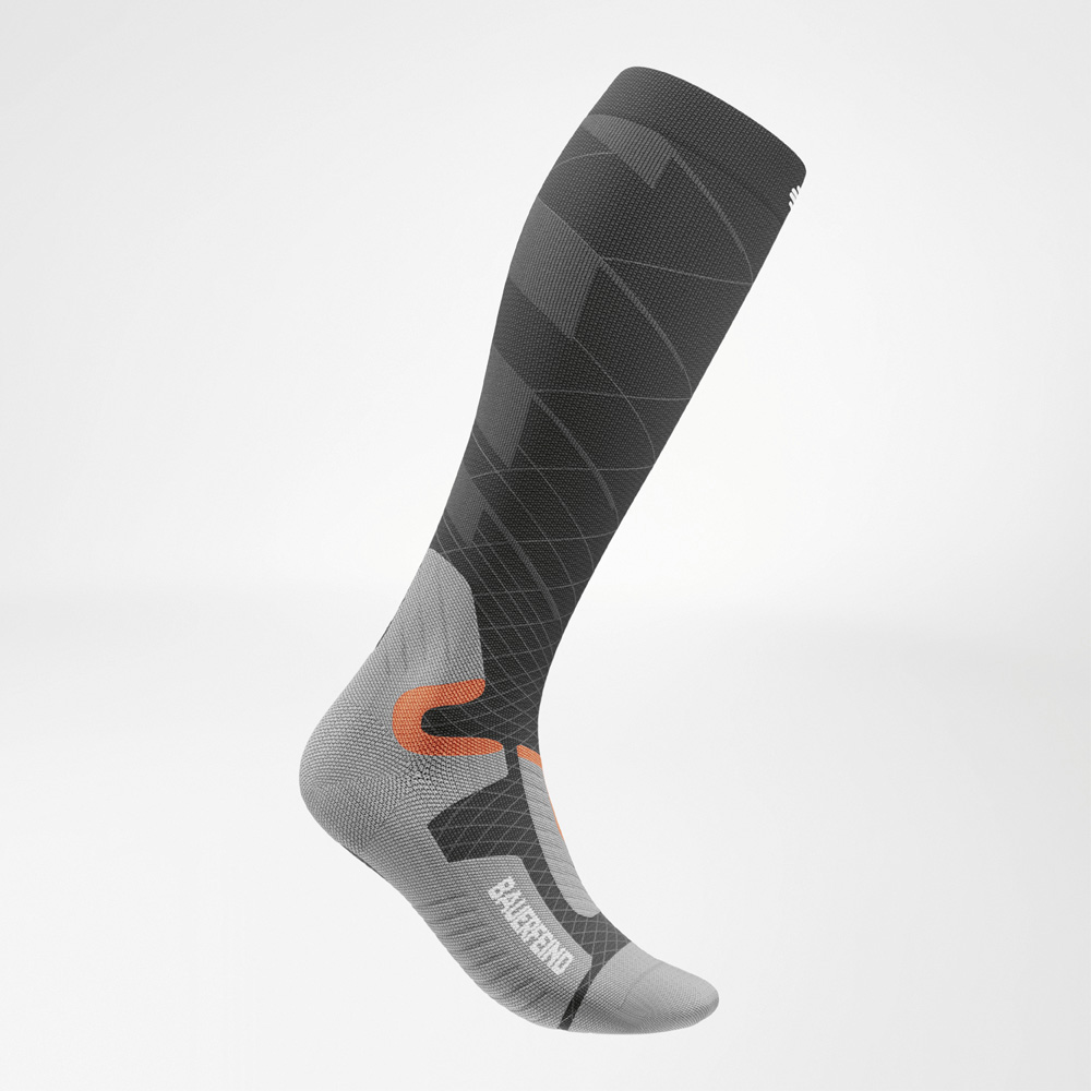 Zijaanzicht van een kniekous van Bauerfeind Sports in antraciet, grijs en oranje. De compressiekous toont een dynamisch lijnpatroon en is anatomisch gevormd naar de voet.