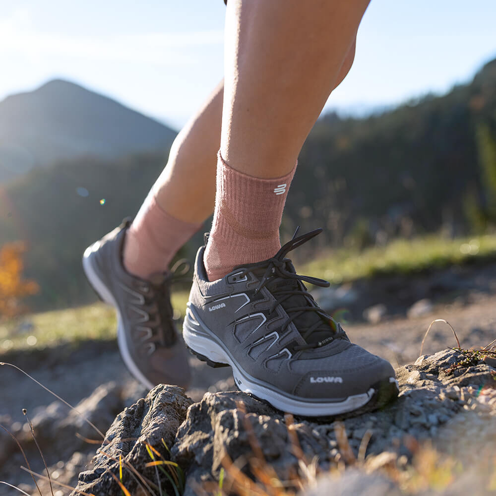 Vrouw met Merino Outdoor Socks in koraalkleur tijdens een bergwandeling. De sokken passen zich perfect aan de voet aan en bieden ademend vermogen en comfort voor lange tochten.