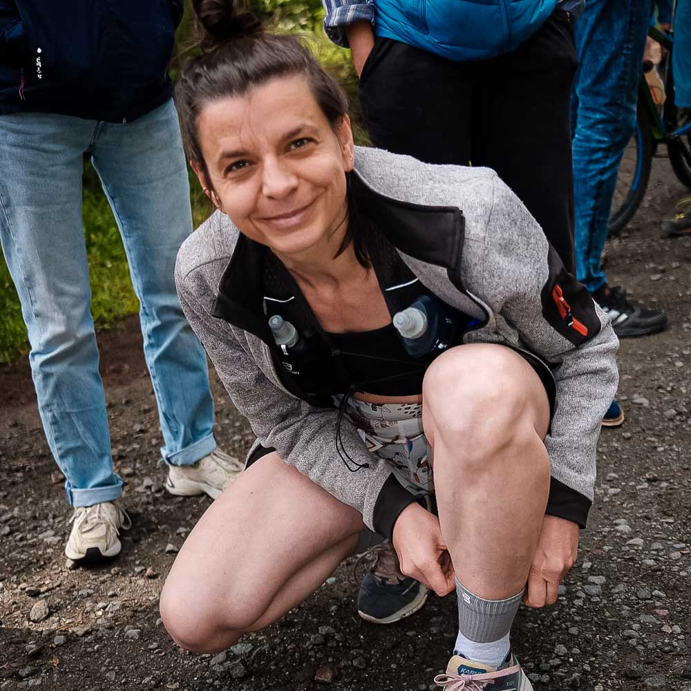Voor de start van de Rennsteiglauf pas je de Trail Run Mid Cut Socks in een goed humeur aan. Een vrouw lacht naar de camera terwijl ze haar halflange sokken verstelt