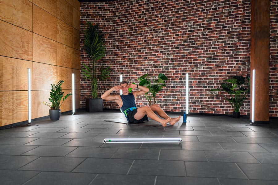 Thomas Röhler maakt een sit-up met een achterband en ligt op een fitnessmat in een kamer vol neonbuizen