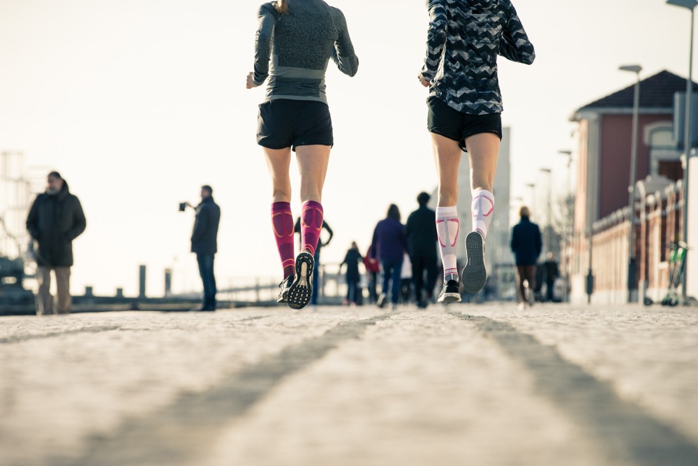 Kikkerperspectief: hardlopers met paarse en witte hardloopsokken lopen door een drukke stad op de achtergrond mensen en lantaarns