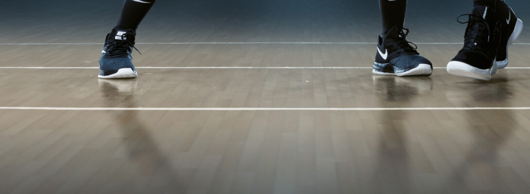 Uitzicht op de vloer van een basketbalzaal en de voeten van twee spelers