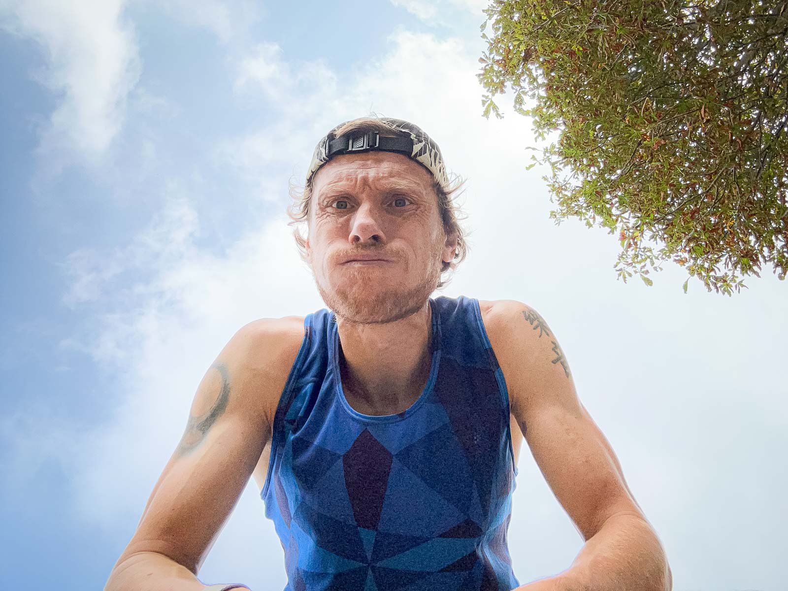 Loper na Training – Uitputting en Succes na het Hardlopen. Close-up van een loper die zwaar ademt na een run. Hij draagt een blauw shirt en een pet, terwijl hij in de camera kijkt.