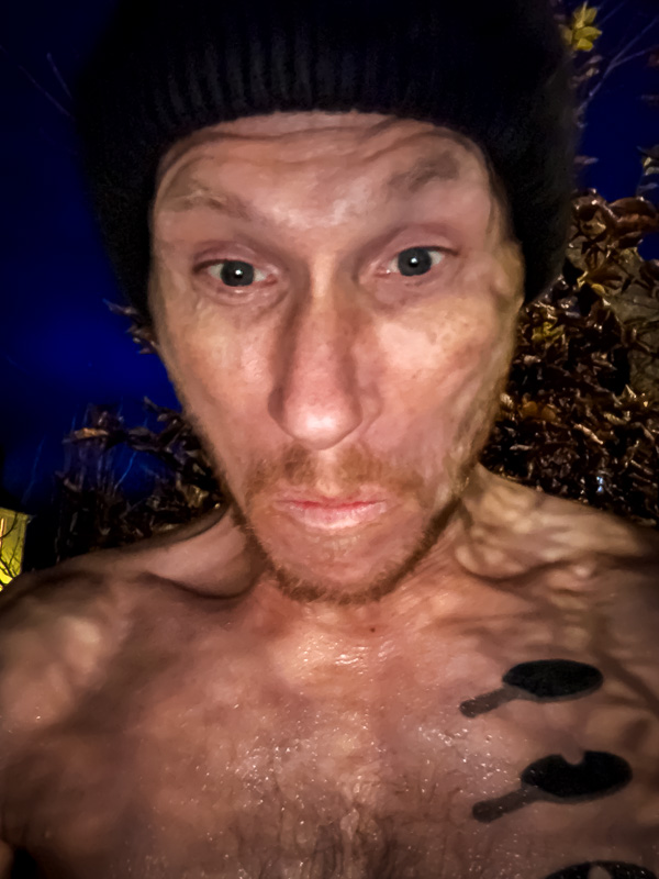 De sprong wagen: Wanneer het ijsbad-gezicht serieus wordt! Een man met een zwarte muts en nat bovenlichaam kijkt gespannen in de camera. De achtergrond toont herfstbladeren tegen een donkere avondlucht.