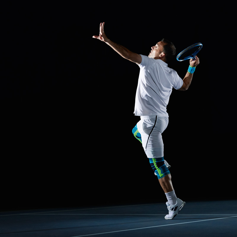 Tennisspeler in witte kleding tegen een zwarte achtergrond op de serve