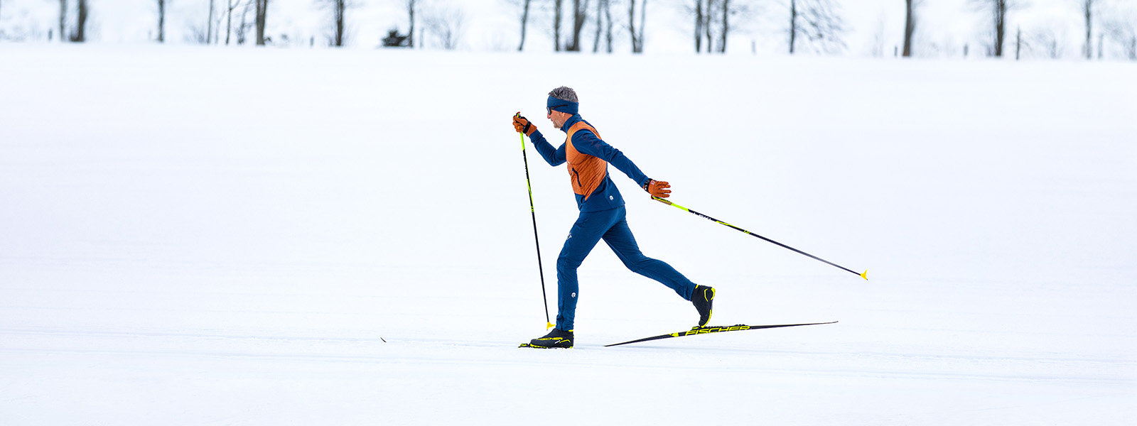 Kleurrijk langlaufen in een winterlandschap Een man in oranje en blauwe kleding langlauft door de sneeuw.