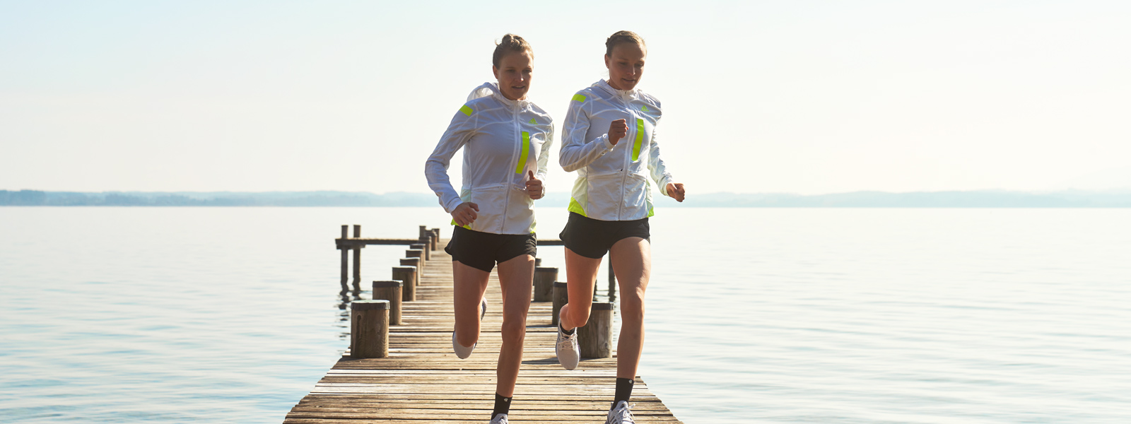 Wanneer de Patella -pees in staking gaat: wat te doen met een Patella Tip -syndroom? Twee lopers in witte hardloopjassen en met korte broek rennen over een steiger naar de bank