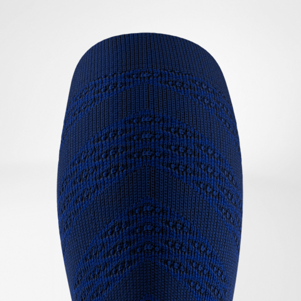 Close-up van een donkerblauwe compressiesleeve met een opvallend V-vormig breipatroon. De stevige stof benadrukt de sportieve look en de functionele ondersteuning voor de kuitspieren.
