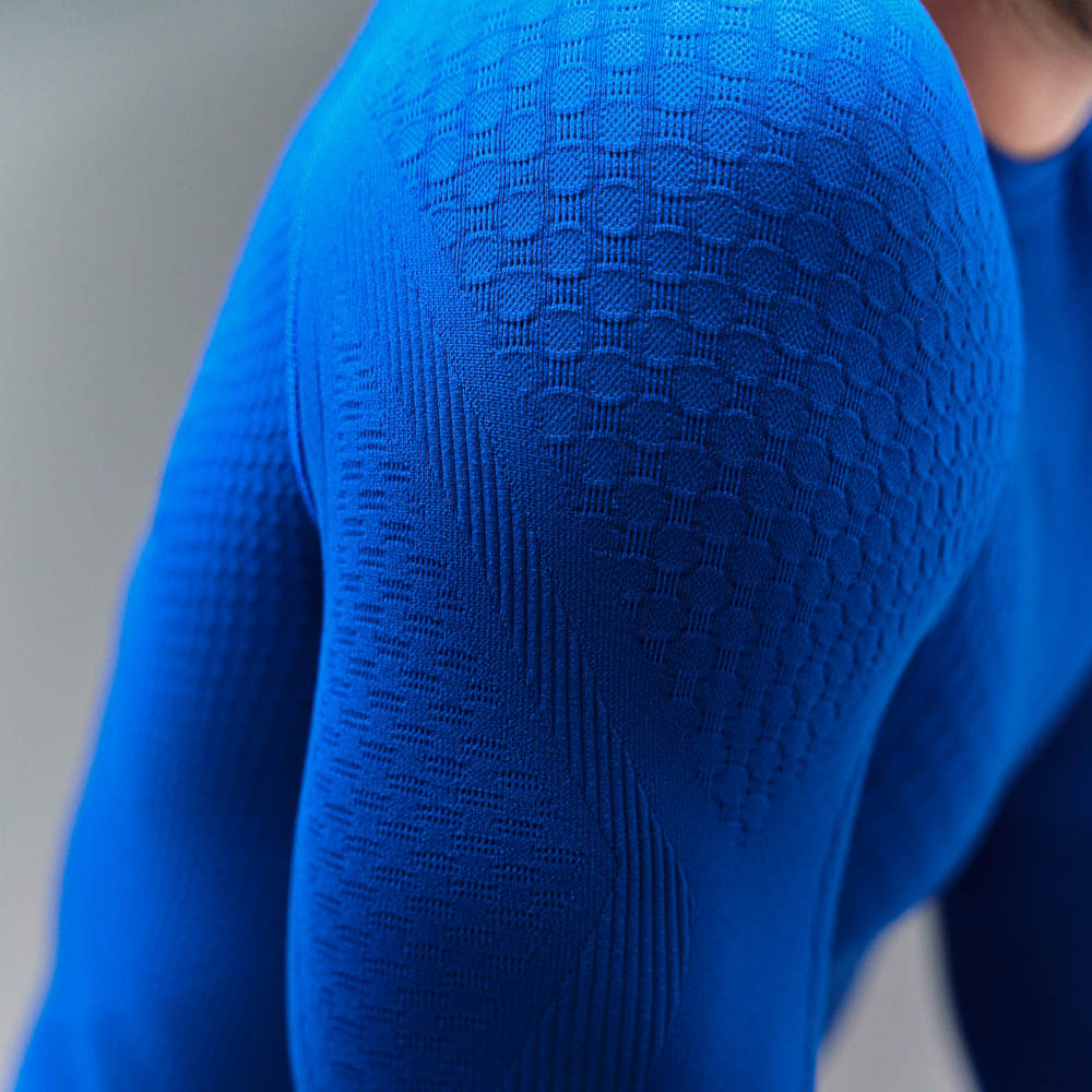 Sporttop van gebreid compressiepatroon dat de spieren benadrukt Gedefinieerde bovenarm van een man die een blauw compressietopje met lange mouwen draagt