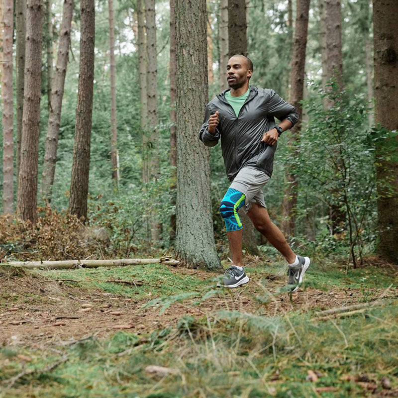 Een hardloper rent dynamisch door het bos en draagt een knieverband