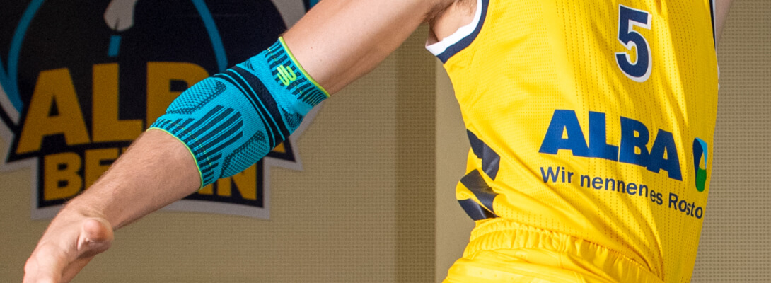 Ellenbogen verband in basketbal Basketbalspeler met Alba Berlin Jersey draagt een sportverband voor de elleboog