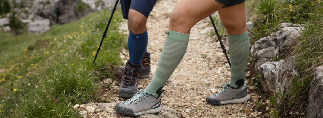 Twee mensen wandelen over rotsen die ze merino -wandelsokken op de achtergrond dragen, zijn bomen te zien