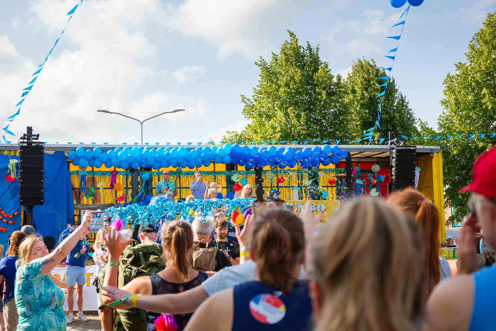 Rijk versierde wagen met blauwe ballonnen en juichende toeschouwers tijdens de 4Daagse in Nijmegen.
