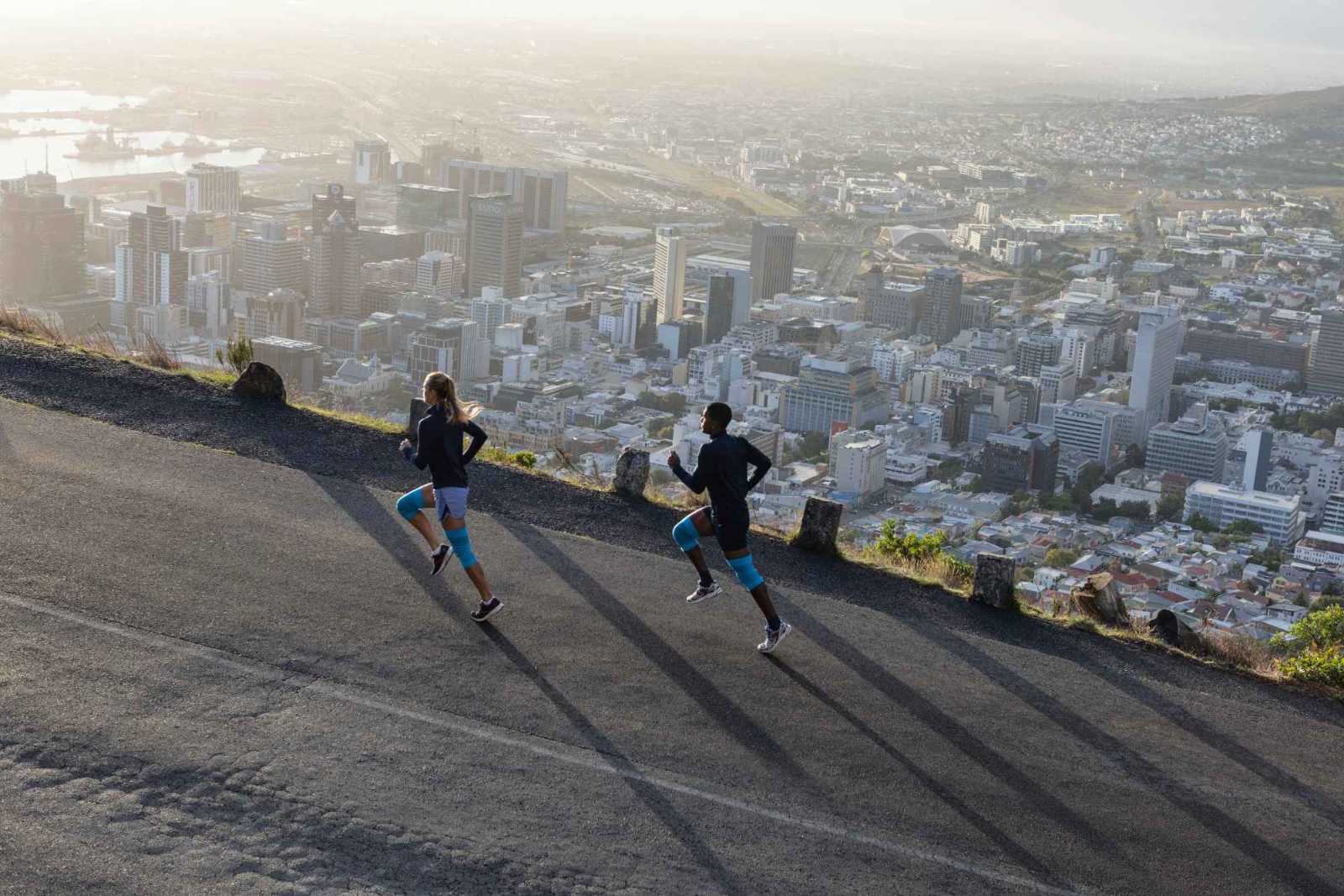 Een vrouw en een man met blauwe kniebars rennen een straat boven een grote stad