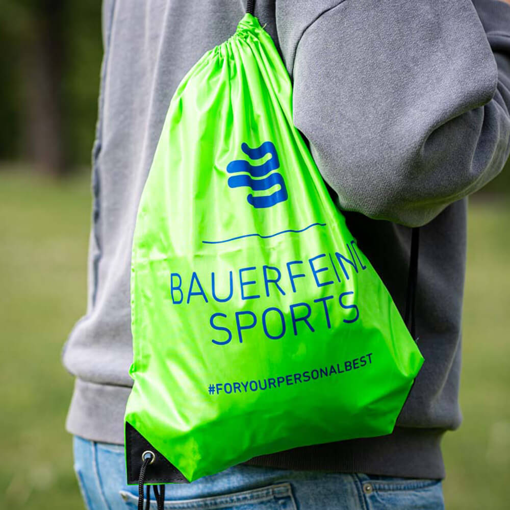 Jouw metgezel: De Bauerfeind Sports gymtas voor onderweg Een persoon draagt een groene Bauerfeind Sports gymtas op de schouder buiten.