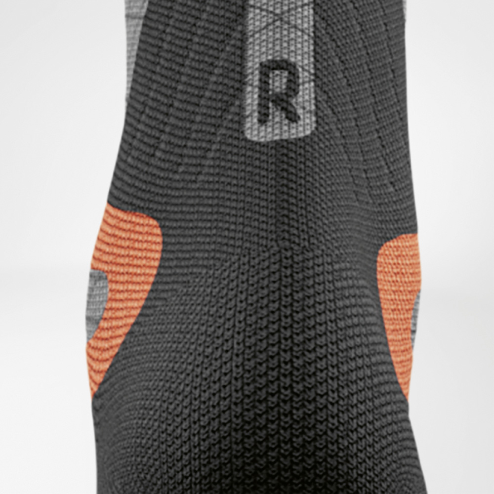 Stabiliteit in elke bocht – rechter hiel met extra demping Detailweergave van de rechter ski-compressiekous voor dames van Bauerfeind. Zichtbaar zijn de oranje hielpads en het zwarte breisel voor gerichte ondersteuning in de schoen.