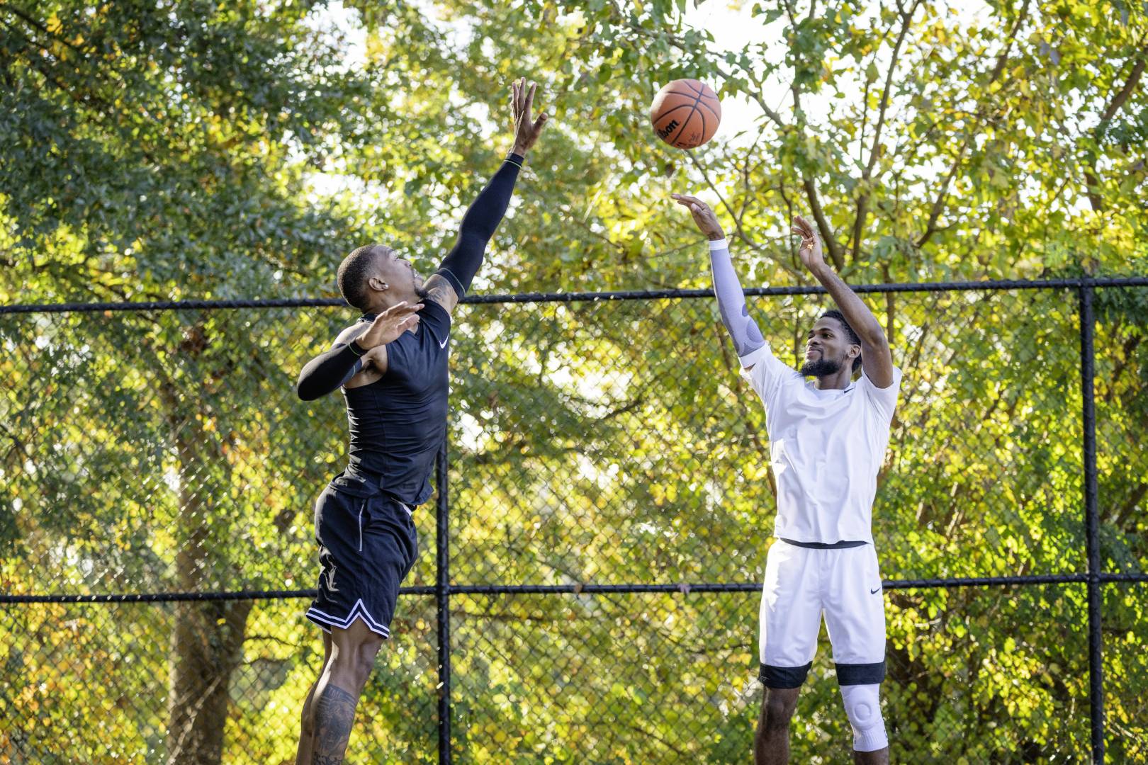 Basketbalspelers in Black Game Clothing proberen zijn tegenstander te blokkeren in witte kleding hoog boven de grond