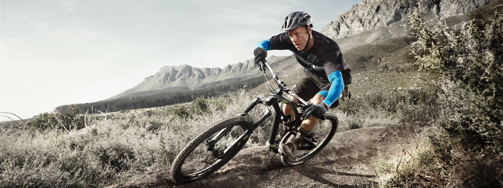 Mountainbiken met arm mouwen Mountainbiker drijft een helling af en draagt blauwe armmouwen